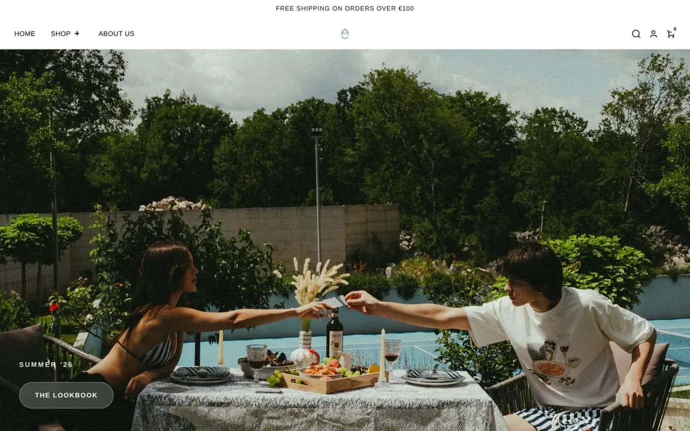 The Raidage Studios homepage: a full-width campaign photograph of two people at a laid table by a pool, with a black-and-white header above it and a “Summer ’26” label over a “The Lookbook” button in the lower left.